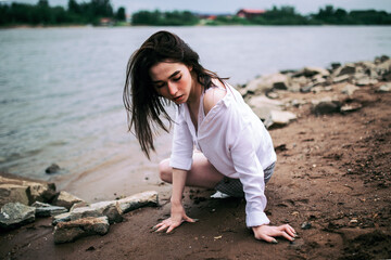 A girl in a white shirt and skirt walks on the stony Bank of the river near the bridge in Ufa