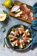 Summer snacks. Pear appetizer with jamon, arugula and brie cheese on a light stone table. Top view flat lay background.