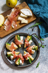 Summer snacks. Pear appetizer with jamon, arugula and brie cheese on a light stone table. Top view flat lay background.