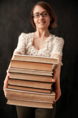 Young girl in glasses smiling and gives a stack of books. Books close-up in hands