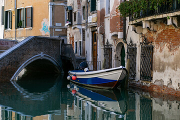 Fototapeta na wymiar horizontal photo of a boat in a venetian canal against the background of an old bridge and flaky brick buildings