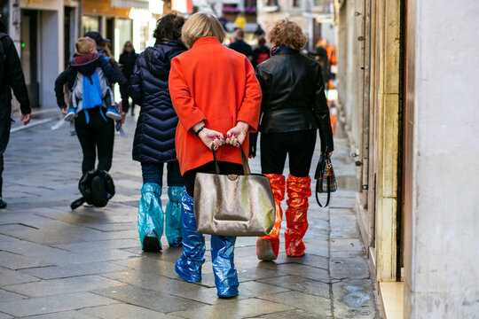 horizontal photo from the back of a group of tourists strolling through Venice in high shoe covers