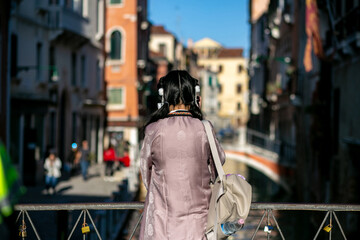 horizontal photo from the back of a girl standing on a bridge on the Venetian canal