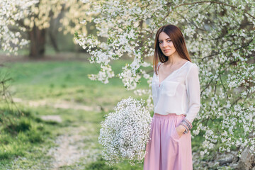 Fototapeta na wymiar Amazing young woman posing in Blooming tree orchard at spring. Beautiful happy young woman enjoying smell in a flowering spring garden