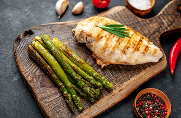 Grilled chicken breast with asparagus and spices on a cutting board on a stone background