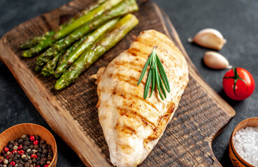 Grilled chicken breast with asparagus and spices on a cutting board on a stone background