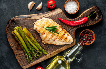 Grilled chicken breast with asparagus and spices on a cutting board on a stone background