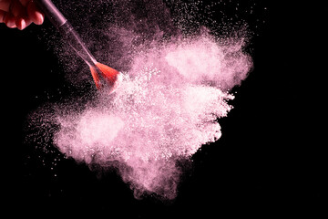 Brush with pink powder explosion on black background.Make-up and beauty concept.
