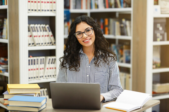 Smiling latina girl using laptop in modern library