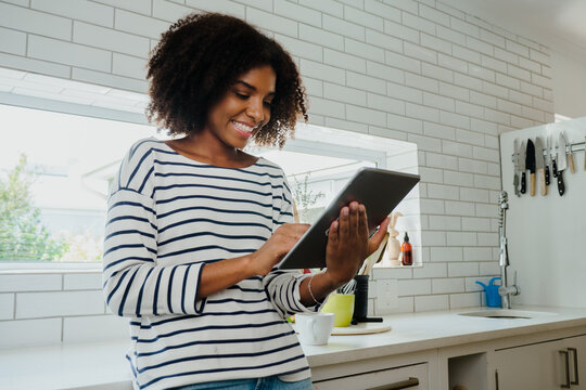 Beautiful young woman scrolling or browsing tablet in the kitchen at home, checking online recipes 