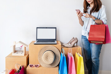Young asian woman with colorful shopping bag, fashion items and stack of cardboard boxes at home, Website online shopping concept with copy space