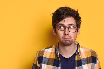 Portrait of sad caucasian man in eyeglasses looking at free copy space for text, information, advertising, isolated on yellow studio wall. Funny guy staring with fear aside. Human emotions concept