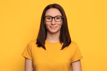 Headshot of glad beautiful lady with dark hair and eyeglasse smiling happily, expresses sincere emotions, dressed in yellow casual t-shirt, model posing in studio alone with mockup space