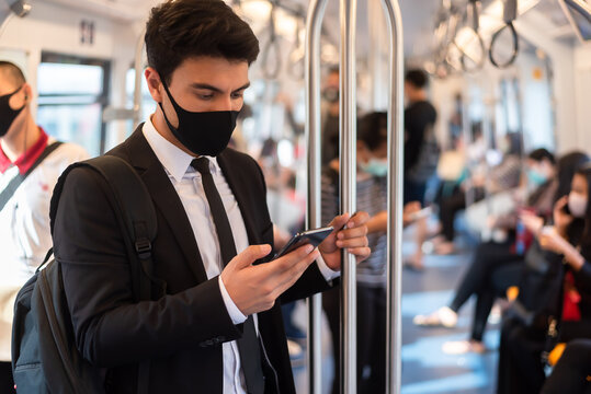 Portrait of confident businessman in black suit wear mask in city finding job during corona crisis using smartphone travelling by train