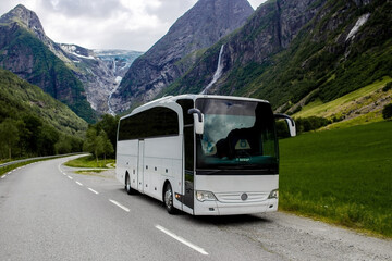 Trip to Norway. Blue ice tongue of Jostedal glacier melts from the giant rocky mountains into the green valley with a lot of waterfalls. Big white tourist bus rides on the road - obrazy, fototapety, plakaty