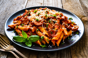 Penne with sausages, tomato sauce, parmesan cheese, basil and vegetables served on wooden table