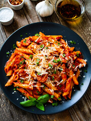 Penne with sausages, tomato sauce, parmesan cheese, basil and vegetables served on wooden table