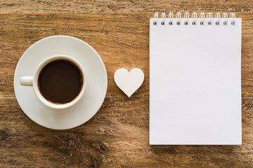 Coffee cup and blank notebook paper on wooden table. Coffee break concept. 