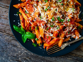 Penne with sausages, tomato sauce, parmesan cheese, basil and vegetables served on wooden table