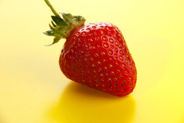 Bright red strawberry on a yellow background close-up.
