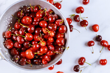 Berry cherries in colander bowl with water drops on white background.