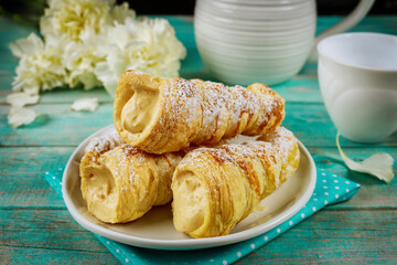 Flaky puff pastry cone with cream and flowers on wooden table.