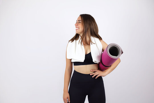 Young beautiful woman standing over white isolated background wearing sport chlotes and working out. Very happy and smailing. She holds a splinter in her hand and a towel around her neck. 