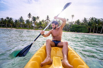 Young man paddling the sea kayak in the tropical calm lagoon.