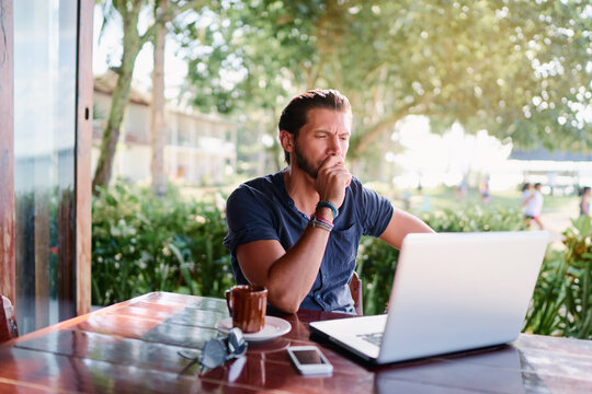 Freelance Concept. Thoughtful Young  Man Using Laptop While Sitting On Cafe Terrace.