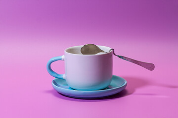 White-blue cup with a saucer and a metal spoon on a purple background.