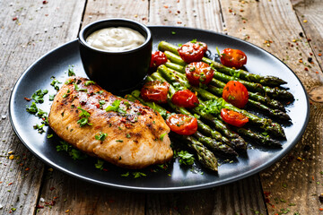Tasty roast chicken breast, green asparagus, cherry tomatoes  and garlic dip on wooden table
