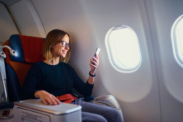 Traveling and technology. Flying at first class. Pretty young businees woman using smartphone while sitting in airplane.