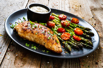 Tasty roast chicken breast, green asparagus, cherry tomatoes  and garlic dip on wooden table
