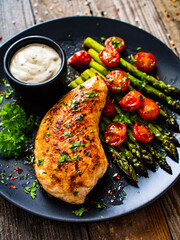 Tasty roast chicken breast, green asparagus, cherry tomatoes  and garlic dip on wooden table
