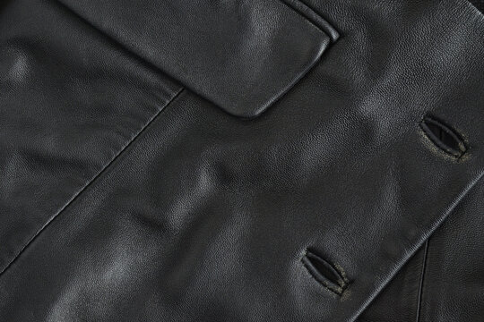 Black genuine worn leather texture with buttonholes and pocket flap. Element of an old vintage jacket. Dark background. Closeup. Focus stacking