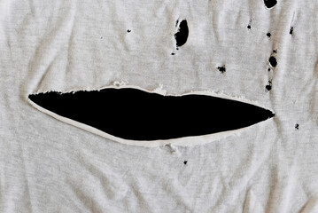 Grunge damaged cloth on black background. Gray white fabric with big hole. Texture of an old dirty...