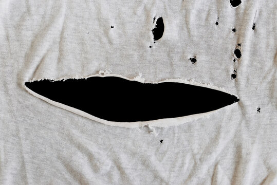 Grunge damaged cloth on black background. Gray white fabric with big hole. Texture of an old dirty ragged t shirt. Copy space