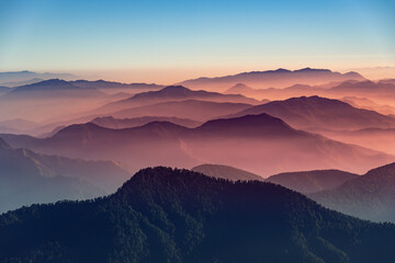 View of Himalayas mountain range with visible silhouettes through the colorful fog from Khalia top trek trail. Khalia top is at an altitude of 3500m himalayan region of Kumaon, Uttarakhand, India. - obrazy, fototapety, plakaty