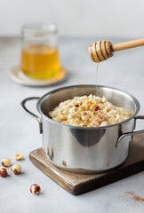 oatmeal porridge with hazelnuts and cinnamon in a pan and a pouring stream of honey. healthy diet breakfast. vertical image. Gray background