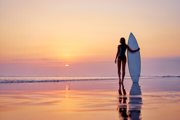 Hobby and vacation. Holiday on the beach. Young woman holding surf board enjoying beautiful sunset.