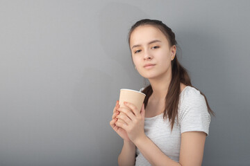 Young woman drinks coffee on gray background