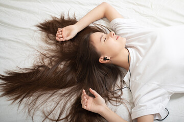 Naklejka premium The girl lies on the bed with a smartphone, listens to the radio with his eyes closed.