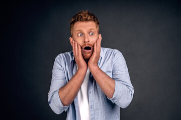 Portrait of funny handsome bearded man with red hair, expressing shock or being terrified of something, standing with opened mouth and popped eyes over gray background. Guy is pale as if he saw ghost