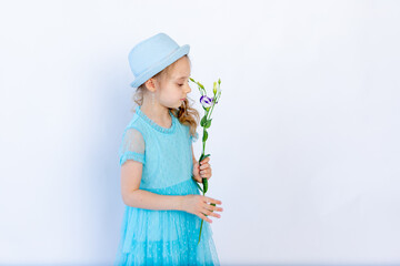 a beautiful 5-6 year old girl in a blue dress sniffs a flower on a white isolated background, space for text