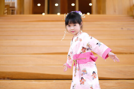 Little asian girl wearing pink traditional japanese dress. Her hair ornaments with flowers. And she is standing on the steps.