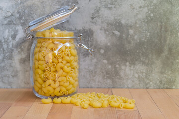 Close-up of Uncooked Macaroni in a glass jar placed on the wooden table background, selective focus. - 355904921