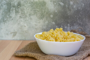Close up of Macaroni in a white bowl placed on the wooden table, selective focus - 355904982