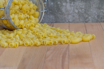Close-up of Uncooked Macaroni in a glass jar placed on the wooden table , selective focus. - 355904984