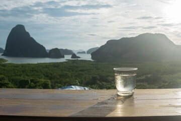 water glass on wood table in the morning sunrise of Samet Nang She is the best and famous view point on Phang nga bay in Southern Thailand. - 355905763