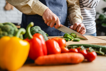 Close up cropped image of mature wife hugging husband while he cooking vegetable salad at home...